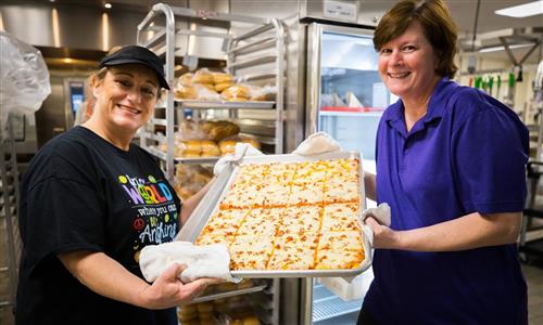 Cafeteria workers hold up pizza 