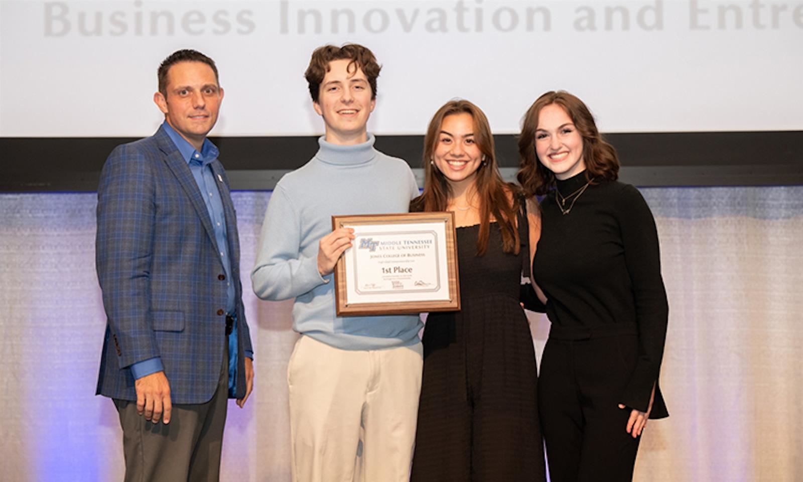 Three students and an adult stand with a plaque
