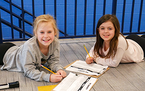  two girls laying on the floor writing on paper