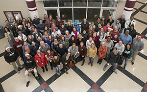  Faculty and staff are dressed for snow. They are standing in the commons area of FHS looking up.