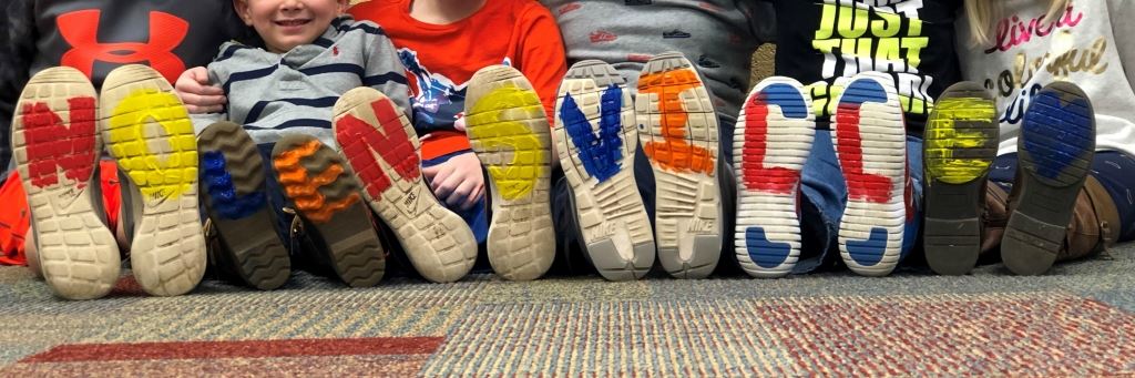 The bottom of kids tennis shoes with writing on each shoe that spells out Nolensville