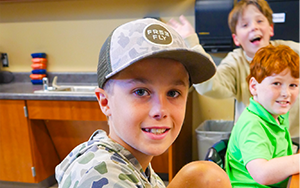  boy with a hat and two boys in the background smiling