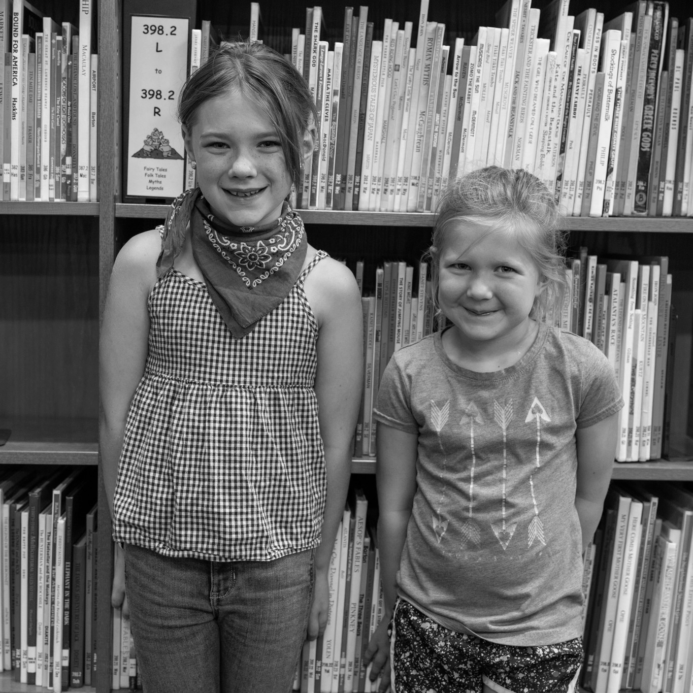 two girls smiling in front of library books