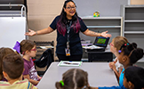  a woman with arms outstretched talking to a table of children