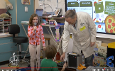 girl talking into microphone with scientist standing next to her