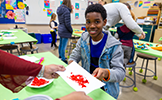  boy smiling while painting with red paint