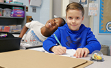  two boys sitting at desks smiling and working