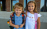  2 children smiling in front of a brick wall