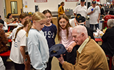  girls talking to a veteran man holding a hat