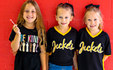  three girls in black shirts against a red wall
