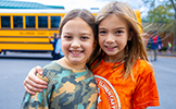 two girls in front of a school bus 