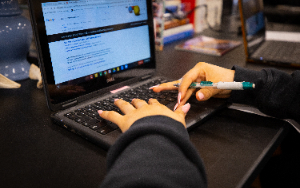  a girl's hands are typing on a chromebook keyboard