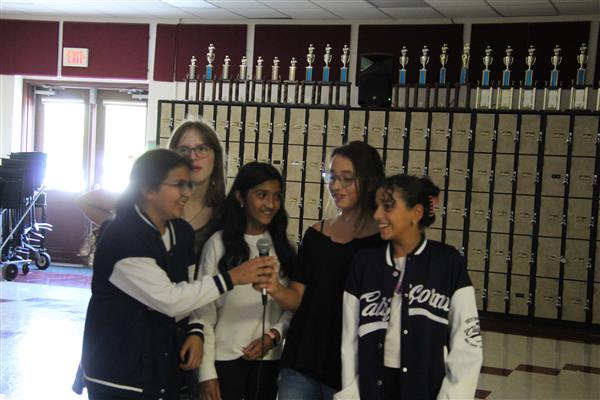 A group of female students sing into a microphone.