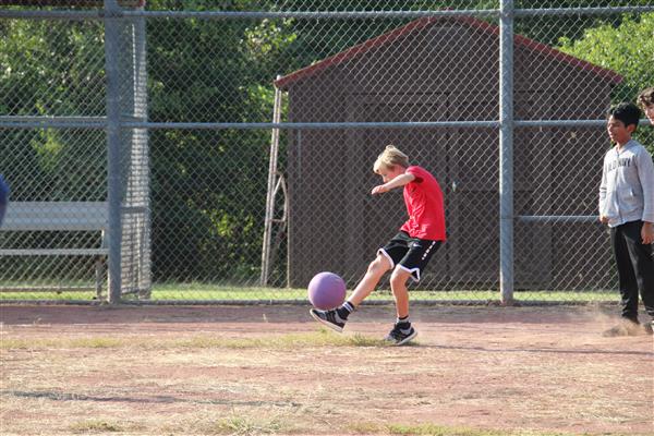 A male student kicks a kickball on a field.